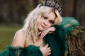 Portrait of A beautiful blonde young woman in a green dress and a diadem on her head in the forest. girl sitting near the old Royalty Free Stock Photo