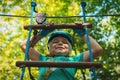 Portrait of a beautiful boy of eleven years in a blue helmet climbing a ladder in a rope park in the summer