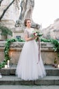 Portrait of beautiful bride in amazing wedding dress holding tender bouquet while standing outdoors in the stairs. Old Royalty Free Stock Photo