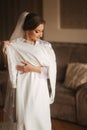 Portrait of beautiful bride standing by the window at home and trying on wedding dress. Charming bride with white Royalty Free Stock Photo