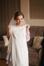 Portrait of beautiful bride standing by the window at home and trying on wedding dress. Charming bride with white Royalty Free Stock Photo