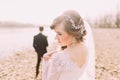Portrait of beautiful bride wearing white dress and veil with groom standing in background near river Royalty Free Stock Photo