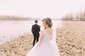 Portrait of beautiful bride wearing white dress and veil with groom standing in background near river Royalty Free Stock Photo