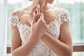 Portrait of beautiful bride in wedding dress with crossed hands standing near window in room, copy space. Bride`s morning Royalty Free Stock Photo