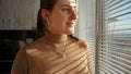 Portrait of beautiful bruentte woman standing by the window with blinds and looking at sunrise