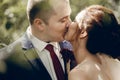 Portrait of beautiful brunette bride kissing handsome groom with red flower boutonniere face close-up, newlywed couple posing Royalty Free Stock Photo