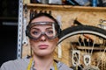 Portrait of a beautiful brunette female wearing working clothes, apron and goggles, standing in a workshop. Royalty Free Stock Photo