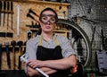 Portrait of a beautiful brunette female wearing working clothes, apron and goggles, standing in a workshop. Royalty Free Stock Photo