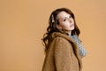 Portrait of beautiful brunette girl in beige fur coat on beige background