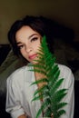 Portrait of beautiful brunette girl with brown eyes with bright green fern in hand close-up Royalty Free Stock Photo