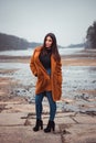 Portrait of beautiful brunette girl woman in orange fashion coat in season with frozen lake on background. Female model in jeans Royalty Free Stock Photo