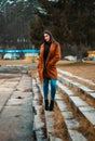 Portrait of beautiful brunette girl woman in orange fashion coat in season - photo on stairs with park and nature on background Royalty Free Stock Photo