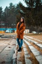 Portrait of beautiful brunette girl woman in orange fashion coat in season - photo on stairs with park and nature on background Royalty Free Stock Photo