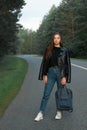 Portrait of beautiful brunette young girl in black leather jacket at sunset walking along the road,