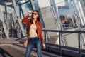 Portrait of beautiful brunette young woman in nice red brown jacket, denim jeans and sunglasses. Genuine leather bag, high heels