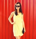 Portrait of beautiful brunette young woman wearing yellow dress, handbag clutch on red background Royalty Free Stock Photo