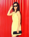 Portrait of beautiful brunette young woman wearing yellow dress, handbag clutch on red background Royalty Free Stock Photo