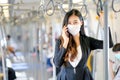 Portrait of beautiful business woman with hygiene mask use mobile phone and stand with hold handrail in sky train. She still work Royalty Free Stock Photo