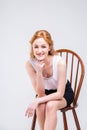 Young beautiful woman with long red, curly hair sitting on a wooden chair on a white background in the studio. Dressed in a white Royalty Free Stock Photo