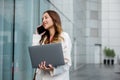 Asian businesswoman working on laptop and talking on cell phone at front building near office Royalty Free Stock Photo