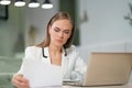 Portrait of a beautiful businesswoman in white jacket working with documents in her hands sitting in front of laptop Royalty Free Stock Photo