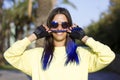 A portrait of beautiful carefree girl with blue hair in yellow top and retro sunglasses in the park looking at camera. funny woman Royalty Free Stock Photo