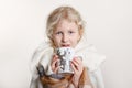 Portrait of beautiful Caucasian girl wrapped in white blanket and drinking from cup. Happy preschool child with blue eyes covered