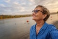 Portrait of  beautiful caucasian happy active senior woman pensioner in a blue shirt  and eyeglasses smiling happily on the river Royalty Free Stock Photo