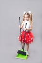 Portrait of a beautiful caucasian little girl cleans the garbage with a broom and dustpan on a gray background