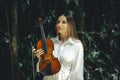 Portrait of beautiful Caucasian woman holding violin in tropical forest. Music and art concept. Female with blond hair wearing Royalty Free Stock Photo