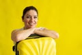 Portrait of a beautiful caucasian woman with a suitcase dreaming of vacation on a yellow background. A smiling girl