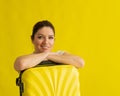 Portrait of a beautiful caucasian woman with a suitcase dreaming of vacation on a yellow background. A smiling girl