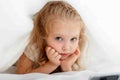 Portrait of beautiful caucasian 5 years girl child hiding in bed. Blonde Kid boring and hides under the cover to watch Royalty Free Stock Photo