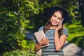 Portrait of beautiful cheerful cute girl holding book talking on phone discussing pastime on fresh air outdoors Royalty Free Stock Photo