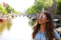 Portrait of beautiful cheerful girl with sunglasses looking to the side upon typical Amsterdam channel, Netherlands, Europe