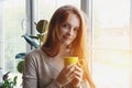 portrait of beautiful cheerful young smiling red hair woman holding yellow coffee cup, enjoying morning coffee at home Royalty Free Stock Photo