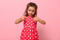 Portrait of beautiful child with positive emotions for advertising. Gorgeous baby girl in pink dress showing thumb up, cute