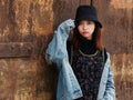 Portrait of a beautiful Chinese girl in blue jeans and black hat posing in front of a rusty door, cute young girl