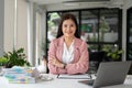 A confident Asian businesswoman sits at her desk with her arms crossed, smiling at the camera Royalty Free Stock Photo