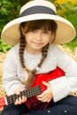 Portrait of a beautiful country girl who plays on the ukulele. Child, music, outdoor.