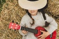 Portrait of a beautiful country girl who plays on the ukulele. Child, music, outdoor.