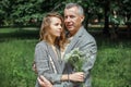 Portrait of beautiful couple gently hugging in green park on sunny day. Adult man and young woman walking with bouquet Royalty Free Stock Photo