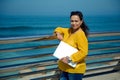 Beautiful curly haired woman with laptop standing against seashore background, holding a laptop and smiling at camera Royalty Free Stock Photo