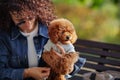 Portrait of beautiful curly haired woman holds small dog Dwarf poodle in arms, while sitting in autumn park. Puppy Royalty Free Stock Photo