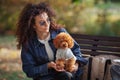 Portrait of beautiful curly haired woman holds small dog on her hands, while sitting in autumn park. Outdoor pet. Toy Royalty Free Stock Photo