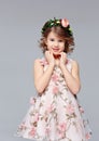 Portrait of a beautiful cut little girl in an elegant dress with a wreath of fresh flowers on her head stands, lauht and looks Royalty Free Stock Photo