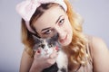 Portrait of a beautiful cute girl with a cat in hands,young woman in a headband for make up on a gray studio background with a