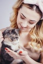 Portrait of a beautiful cute girl with a cat in hands,young woman in a headband for make up on a gray studio background with a