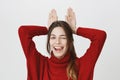 Portrait of beautiful cute girl winking and sticking out her tongue, holding hands above head imitating bunny, isolated Royalty Free Stock Photo