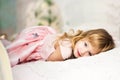 Portrait of beautiful cute little 3 years old blond girl with blue eyes lying on bed in pink dress. Moment of relaxation for Royalty Free Stock Photo
